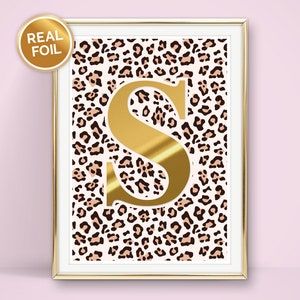 May include: Gold letter S on a white background with a brown and pink leopard print. The letter S is framed in a gold frame.