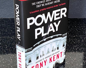 Puede incluir: Una portada de libro en blanco y negro con el título "POWER PLAY" en letras blancas grandes. El nombre del autor, "TONY KENT", está impreso en letras rojas debajo del título. La portada del libro presenta una foto de la Casa Blanca.