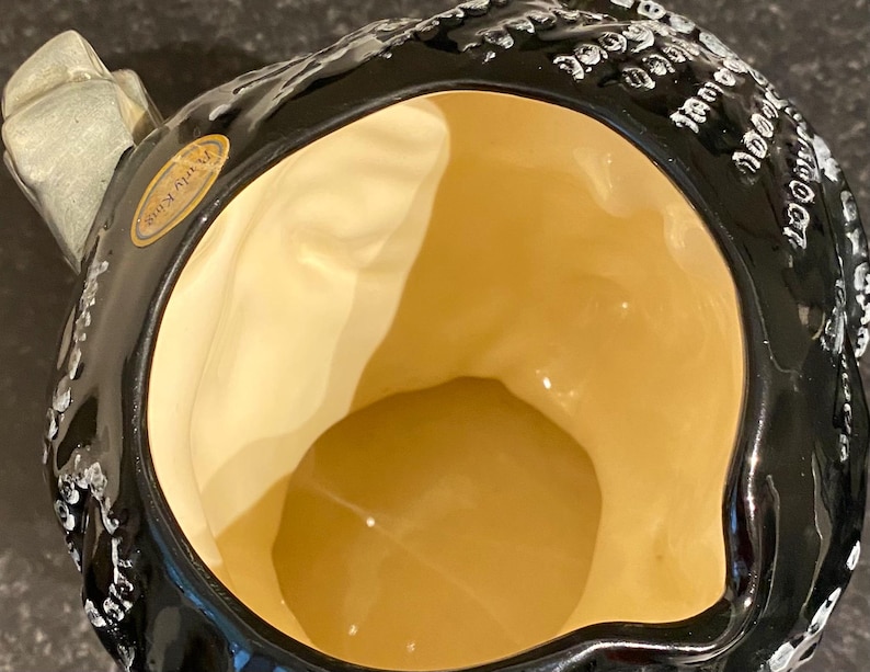 May include: Black ceramic pitcher with white decorative details and a gold interior. The pitcher has a handle and a label that reads "Touraine".