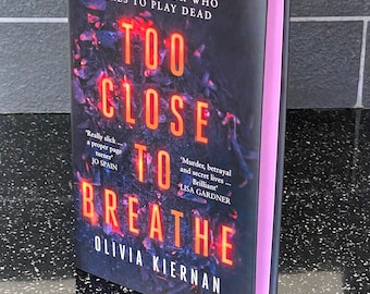 Puede incluir: Una portada de libro con un fondo oscuro y texto rojo que dice "Too Close To Breathe". El libro se titula "Too Close To Breathe" de Olivia Kiernan. La portada presenta una cita de Lisa Gardner que dice "Murder, betrayal and secret lives... Brilliant."
