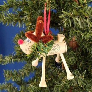 Handmade Wine Cork Reindeer Christmas Ornament. Wine corks and golf tees form the body of these festive deer. Each has greenery around his neck, googly eyes, and a red nose. Pipe cleaners form the antlers and each hangs from a red ribbon.