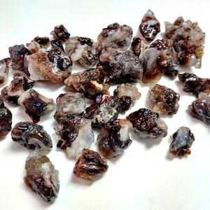 Puede incluir: Una colección de piedras de ágata marrón, blanca y gris de diversas formas y tamaños. Las piedras tienen una textura natural y rugosa.