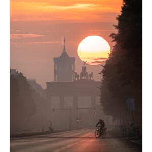 Peut inclure: Une page de calendrier mural pour ao&ucirc;t pr&eacute;sentant une photographie de la porte de Brandebourg &agrave; Berlin au lever du soleil. Le soleil est un grand orbe orange derri&egrave;re le monument, avec la silhouette d'une personne &agrave; v&eacute;lo sur la route.