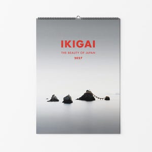 Peut inclure: Un calendrier mural avec une reliure à spirale en haut, présentant une photographie de rochers sombres dans une mer calme et brumeuse. Le texte IKIGAI, THE BEAUTY OF JAPAN et 2027 est imprimé en rouge au centre de la couverture grise et blanche.