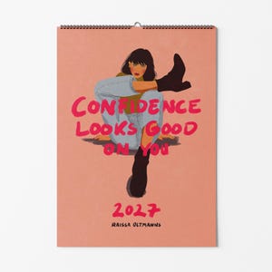 Könnte beinhalten: Ein Wandkalender für 2027 mit pfirsichfarbenem Hintergrund und einer Illustration einer Person in hellblauer Jeans und schwarzen Stiefeln. Der Text lautet: CONFIDENCE LOOKS GOOD ON YOU, 2027 und RAISSA OLTMANNS in fetter, pinker Schrift.