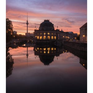 Peut inclure: Une page de calendrier pour juillet pr&eacute;sentant une photographie du mus&eacute;e Bode &agrave; Berlin au coucher du soleil, avec la tour de t&eacute;l&eacute;vision visible au loin. Le b&acirc;timent est illumin&eacute; et se refl&egrave;te dans l'eau calme sous un ciel rose et orange.