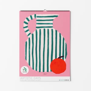 Può includere: Un calendario da parete con sfondo rosa raffigurante una grande brocca bianca con strisce verticali verde scuro e un manico. Un frutto arancione a tinta unita si trova in basso a destra. Il testo recita ARTISTIC DAYS A BETTER WORLD IN 2027 e PHOTOCIRCLE.