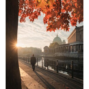 Peut inclure: Une page de calendrier pour octobre pr&eacute;sentant une photographie d'une personne marchant le long d'une rive au coucher du soleil. La sc&egrave;ne comprend un arbre aux feuilles d'automne rouge vif, un d&ocirc;me au loin et une rambarde m&eacute;tallique.