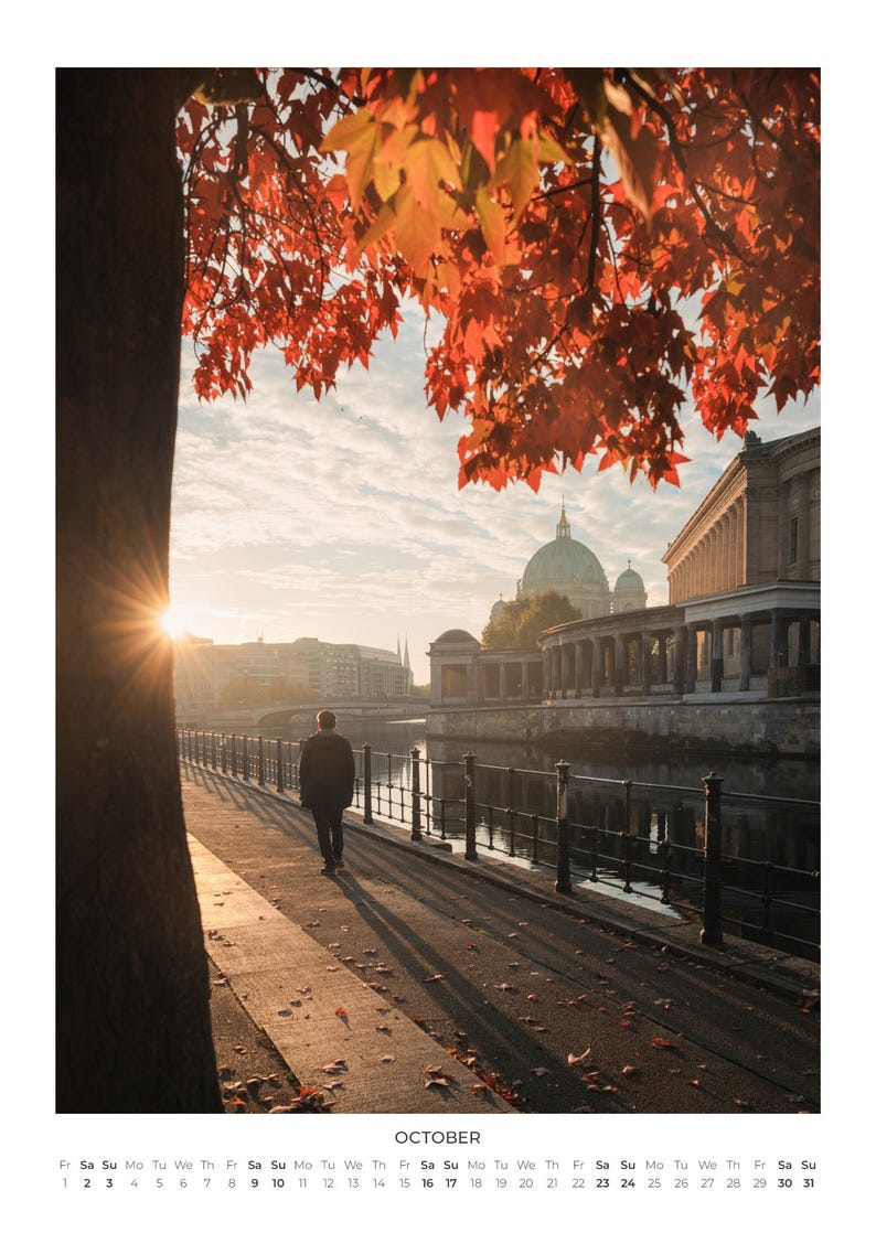Peut inclure: Une page de calendrier pour octobre pr&eacute;sentant une photographie d'une personne marchant le long d'une rive au coucher du soleil. La sc&egrave;ne comprend un arbre aux feuilles d'automne rouge vif, un d&ocirc;me au loin et une rambarde m&eacute;tallique.