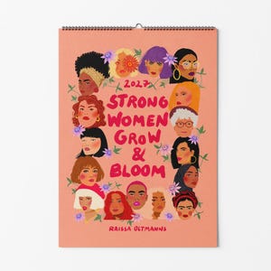 Peut inclure: Un calendrier mural 2027 sur fond pêche avec le texte Strong Women Grow & Bloom et Raissa Oltmanns. Le design présente un arrangement central de visages illustrés divers entourés de petits accents floraux violets et verts.