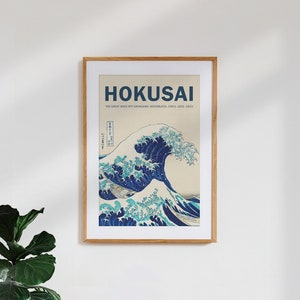 Puede incluir: Una impresión enmarcada de "La Gran Ola de Kanagawa" de Hokusai. La impresión presenta una gran ola azul con el monte Fuji en el fondo. El título "Hokusai" y el texto "La Gran Ola de Kanagawa, Xilografía, Circa 1829-1833" están impresos debajo de la imagen.