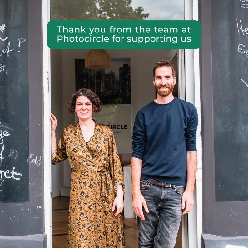 Peut inclure: Deux personnes debout dans une porte avec un panneau vert au-dessus indiquant Thank you from the team at Photocircle for supporting us. Une personne porte une robe portefeuille longue &agrave; motifs marron, l'autre un sweat bleu marine et un jean.