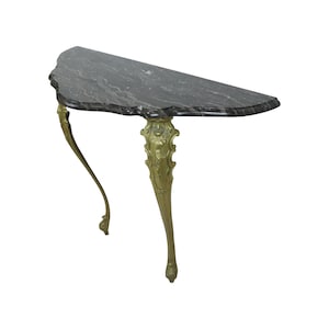 Op de afbeelding: Een halfronde marmeren consoletafel met sierlijke, goud geverfde poten. Het tafelblad is zwart met witte aderen.