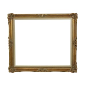 May include: Ornate gold picture frame with detailed carvings on the corners and edges. The frame has a rectangular shape with a white interior, perfect for displaying artwork or photographs. The frame is made of a gold-colored material.