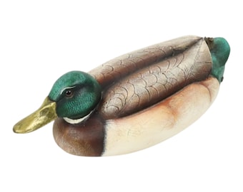May include: A detailed duck figurine, hand-painted with a green head, yellow beak, and brown and tan feathers. The duck is depicted lying down, highlighting the intricate craftsmanship and realistic details of the sculpture.