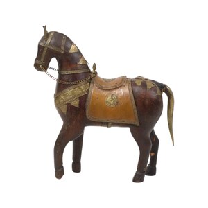 Pode incluir: Escultura de cavalo de madeira com sela e freio. O cavalo é marrom com detalhes em metal dourado na sela, freio e corpo. A sela é bege e tem um emblema decorativo.