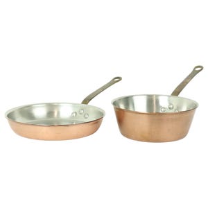 May include: Two copper pots with brass handles. The pot on the left is a frying pan and the pot on the right is a saucepan.