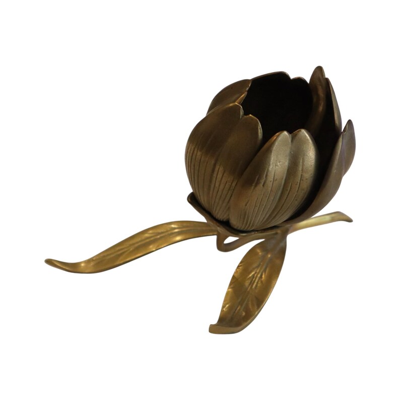 Op de afbeelding: Een koperen kandelaar in de vorm van een bloeiende bloem met een centrale cup voor een kaars, omringd door gelaagde bloemblaadjes. De basis heeft een lange, slanke steel met twee uitgestrekte bladeren, alles in een gouden metaalkleur.
