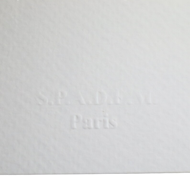 May include: A white label with the text "S.P.A.D.A. Paris" embossed in black.