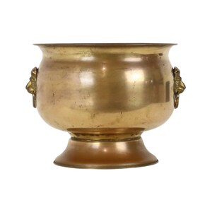 May include: A polished brass bowl with a wide, flared rim and a pedestal base. The vessel features two decorative handles on opposite sides, each shaped like a lion head with a ring attached, showcasing a metallic gold finish and smooth surface.