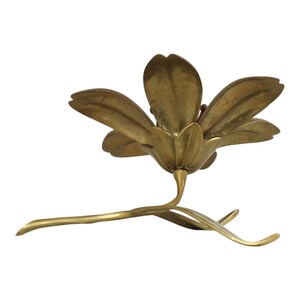 Op de afbeelding: Een koperen bloemensculptuur met zes gladde, afgeronde bloemblaadjes in een bloeiende vorm. De bloem is bevestigd aan een gebogen, slanke stengel die horizontaal uitsteekt en een stabiele basis vormt voor het metalen bloemstuk om op te rusten.