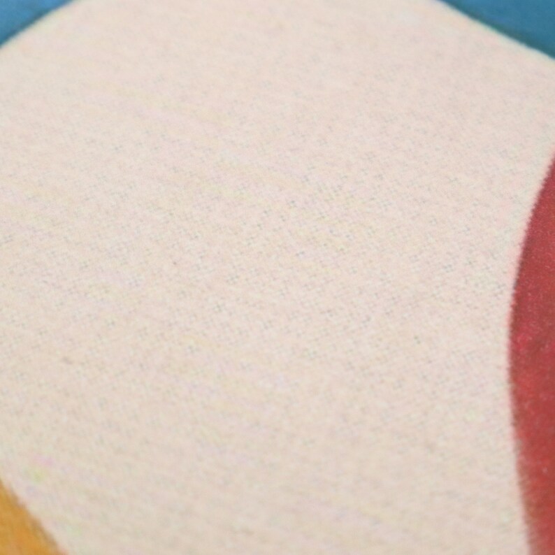 May include: A close-up of a cream-colored fabric with a subtle texture. The fabric is part of a larger design with a red, orange, and blue color scheme.