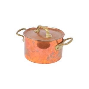 May include: A copper pot with brass handles and a lid. The pot has a slightly tarnished finish.