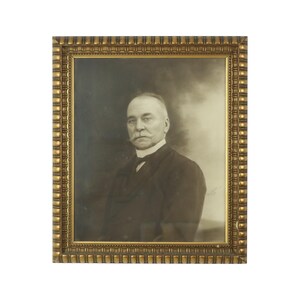 May include: A black and white portrait of a man in a suit and tie, framed in a gold ornate frame.