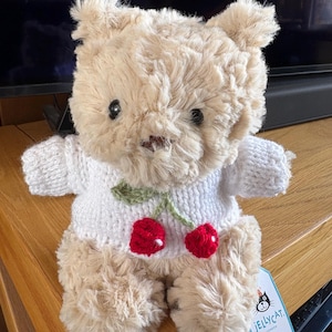 May include: A white ceramic mug with a black handle and the text "But First, Coffee" in a black, bold font. The mug is on a white surface.