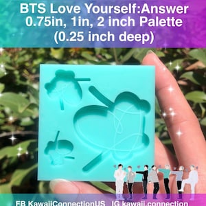 May include: A blue silicone mold with three different shapes of the BTS Love Yourself: Answer logo. The mold is 0.75 inches, 1 inch, and 2 inches wide and 0.25 inches deep. The mold is held in a hand against a green leafy background.