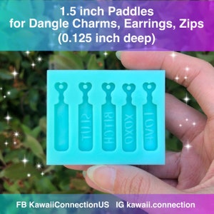 May include: A blue silicone mold with four paddle-shaped cavities. Each cavity has a heart-shaped top and a different word inscribed: "TU12", "BILCH", "OXOX", and "LOVE".