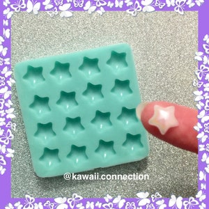 May include: A square mint green silicone mold featuring sixteen star-shaped cavities arranged in a grid. A single small, iridescent, star-shaped piece is shown separately. The text @kawaii.connection is printed at the bottom of the mold.