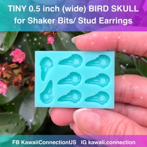 以下が含まれることがあります： ターコイズブルーのシリコンモールドで、6つの鳥の頭蓋骨の形が作られています。それぞれの幅は0.5インチです。モールドは、ピンクの花と緑の葉を背景に、手で持たれています。画像の上部には「TINY 0.5 inch (wide) BIRD SKULL for Shaker Bits/ Stud Earrings」というテキストが書かれています。画像の下部には「FB KawaiiConnectionUS IG kawaii.connection」というテキストが書かれています。