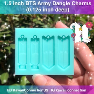 May include: A light blue silicone mold with four cavities for making 1.5 inch BTS Army dangle charms. The mold is 0.125 inches deep. The mold is held in a hand.