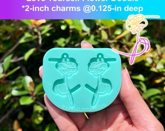Puede incluir: Un molde de silicona turquesa para hacer dos abalorios de flores de 5 cm. El molde tiene forma de flor con tallo y hojas. El molde tiene una profundidad de 0,3 cm. El texto "Love Yourself Flower Doodle" y "@kawaii.connection" está impreso en el molde.