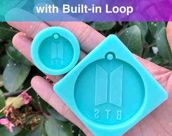 May include: Two silicone molds for making resin keychains featuring the BTS logo. The larger mold is 2 inches in diameter and the smaller mold is 1 inch in diameter. Both molds have a built-in loop for attaching to a keychain.