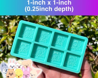 May include: A teal silicone mold with eight square cavities. Each cavity has a raised design of a cartoon animal with the name of a member of the K-pop group Stray Kids written underneath. The mold is 1 inch by 1 inch and 0.25 inches deep.