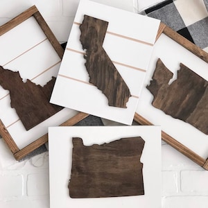 May include: Four wooden state outlines in frames, each with a white background and a brown wooden frame. The states are Idaho, California, Washington, and Oregon.