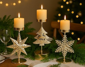 May include: Three gold-colored candle holders with lit candles. The candle holders are shaped like a star, a Christmas tree, and a snowflake. The candles are ivory-colored. The scene is set on a table with greenery and a Christmas tree in the background.