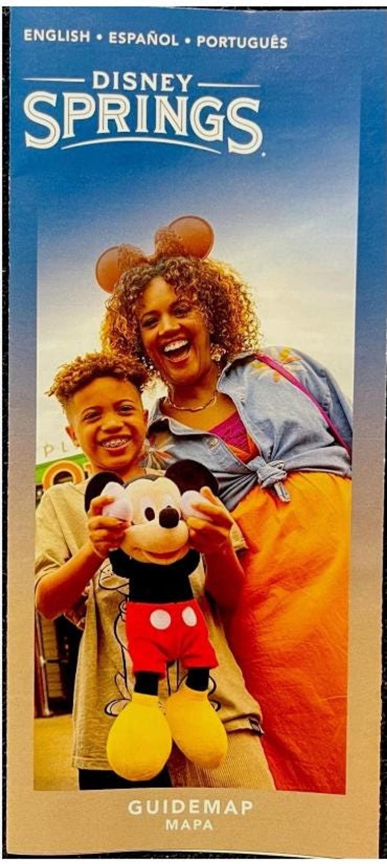 A Disney Springs multigraph guidemap brochure showing a smiling boy holding a Mickey Mouse plush toy next to a woman.