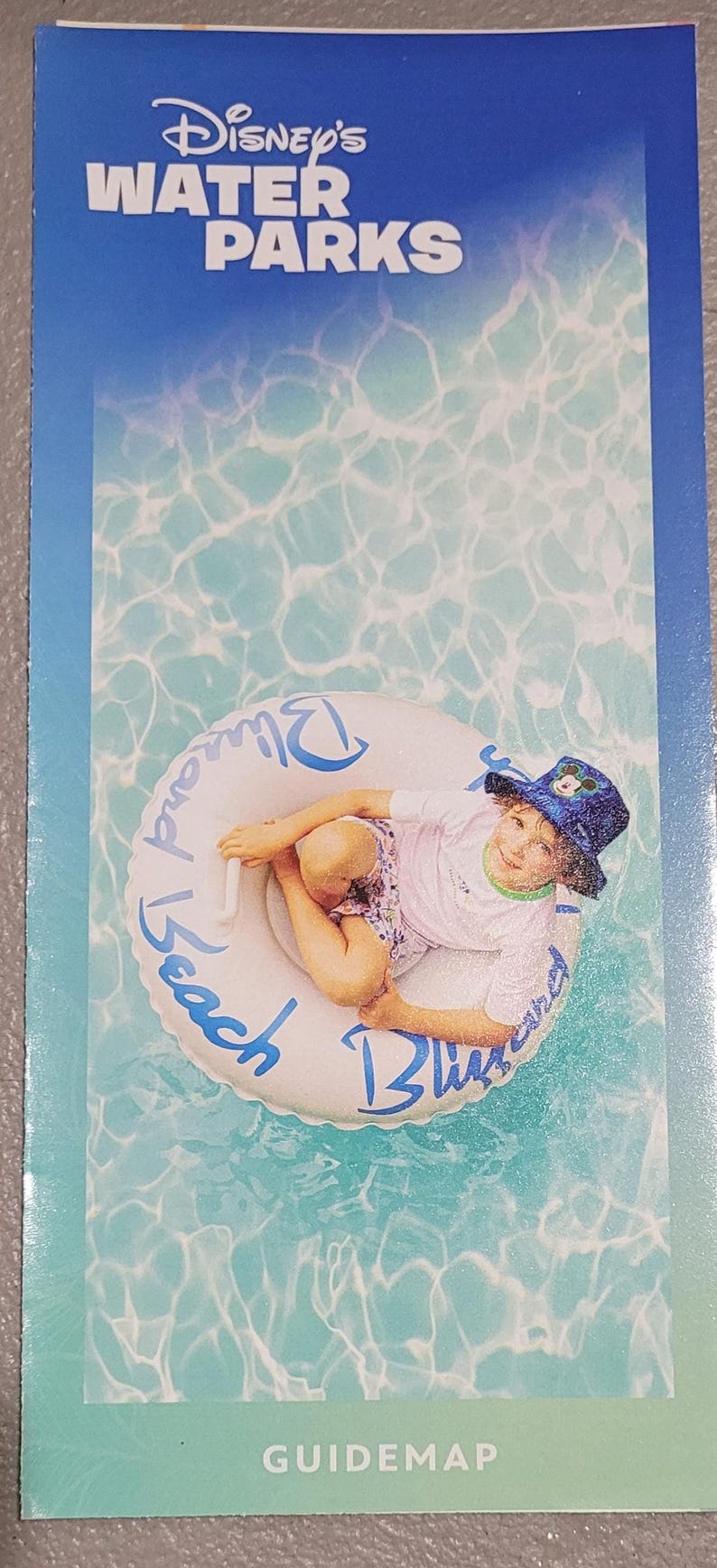 A vertical guide map brochure for Disney's Water Parks features a child in a hat floating in a tube on blue water.
