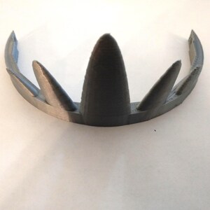 A gray 3D-printed crown featuring five graduated triangular spikes on a flat white surface viewed from the front and slightly above.