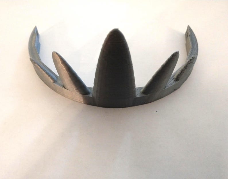 A gray 3D-printed crown featuring five graduated triangular spikes on a flat white surface viewed from the front and slightly above.