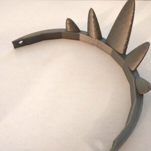 An angled top-down view of a gray 3D-printed crown showing its curved band and layered print texture on a plain background.