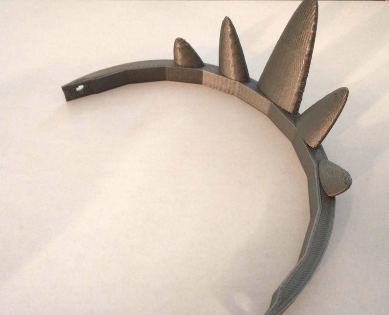 An angled top-down view of a gray 3D-printed crown showing its curved band and layered print texture on a plain background.