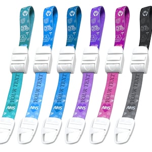 Peut inclure: Six lanyards de différentes couleurs, dont le turquoise, le bleu, le violet, le rose et le gris. Chaque lanyard est doté d'un fermoir en plastique blanc et d'une sangle avec le texte "YOUR TEXT" et "NHS". Les sangles affichent également un symbole d'ambulance et de cœur.