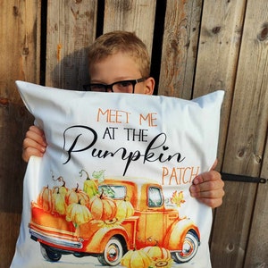 May include: White square cushion with the text "Meet Me at the Pumpkin Patch." The cushion features an orange vintage truck filled with pumpkins. The design includes autumn leaves and pumpkins in shades of orange and yellow.