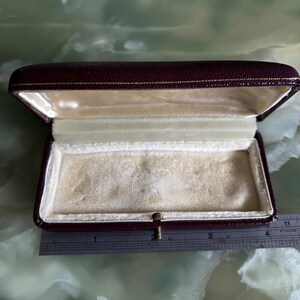 Peut inclure: Une boîte à bijoux en velours bordeaux avec un fermoir doré. La boîte est ouverte et l'intérieur est doublé de velours blanc.