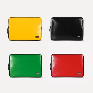 May include: Four laptop sleeves in different colors: yellow, black, green, and red. Each sleeve has a zipper and a small black label with the word "LNDSCPN" on it.