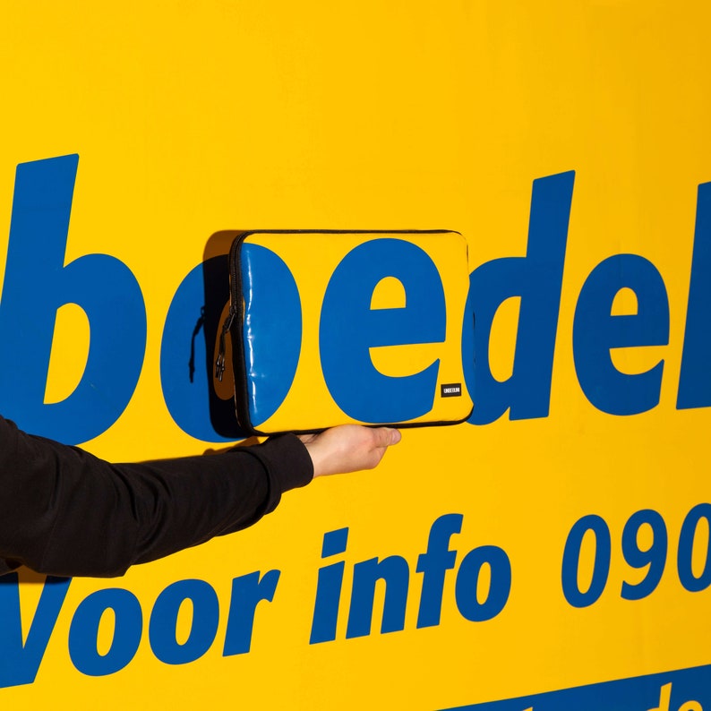 May include: A blue and black laptop sleeve with the word "boedel" in blue letters on a yellow background. The text "voor info 090" is also visible in blue letters.
